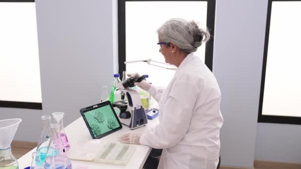 研究室では顕微鏡で見た胚の画像を用いて科学者の制服を着た中世の白髪の女性 — ストック動画