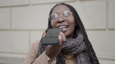 African woman sending voice message with phone at street