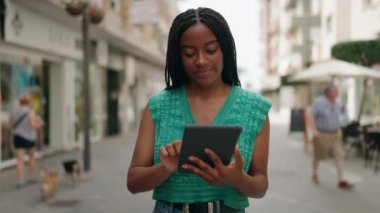 Sokakta yürürken dokunmatik ped kullanan Afro-Amerikan kadın gülümsüyor