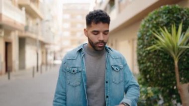 Young arab man with relaxed expression looking watch walking at street