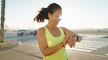 Middle age woman wearing sportswear smiling confident looking stopwatch at street