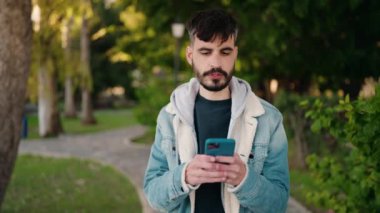 Genç İspanyol adam gülümsüyor. Parktaki akıllı telefonun yanında özçekim yapıyor.