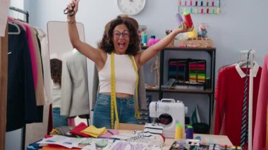 Middle age woman tailor smiling confident holding scissors and thread at clothing factory
