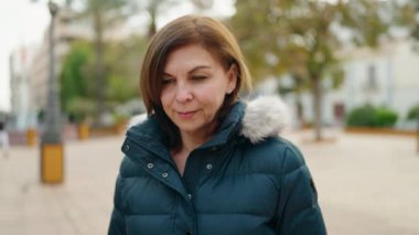 Orta yaşlı bir kadın parkta kendine güvenerek gülümsüyor.