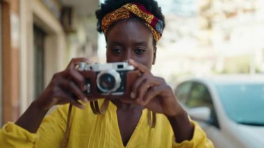 Young african american woman smiling confident using vintage camera at street