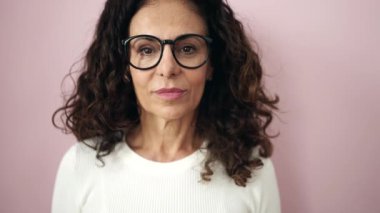 Orta yaşlı İspanyol kadın pembe arka planda kendine güvenen bir şekilde gülümsüyor.