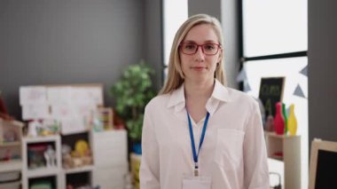 Young blonde woman preschool teacher smiling confident standing with arms crossed gesture at kindergarten