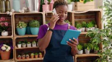 Çiçekçide dokunmatik ped kullanarak akıllı telefondan konuşan Afrikalı Amerikalı kadın çiçekçi.