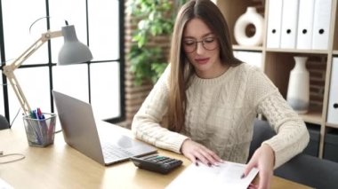 Young beautiful hispanic woman business worker using laptop reading document at office