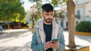 Genç İspanyol adam gülümsüyor. Parktaki akıllı telefonun yanında özçekim yapıyor.