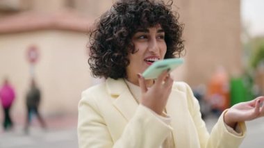 Gülümseyen genç bir kadın caddedeki akıllı telefondan konuşuyor.