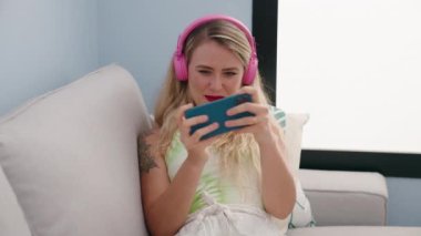 Evdeki kanepede oturmuş video oyunu oynayan genç ve güzel İspanyol kadın.