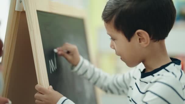 Adorable Hispanic Boy Preschool Student Writing Blackboard Classroom — Video