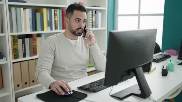Young Hispanic Man Student Using Computer Talking Smartphone Library University — Vídeo de stock