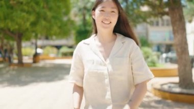 Çinli bir kadın parkta yürürken kendine güvenerek gülümsüyor.