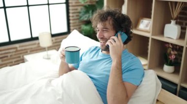 Genç İspanyol adam akıllı telefonda konuşuyor. Yatak odasında kahve içiyor.