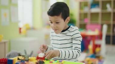 Adorable hispanic boy playing with construction blocks standing at kindergarten