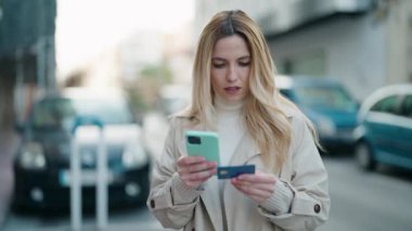 Sokakta akıllı telefon ve kredi kartı kullanan genç sarışın kadın.