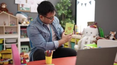 Young chinese man preschool teacher having online vocabulary lesson at kindergarten