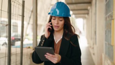 Latin kökenli genç bir mimar, elinde touchpad ile akıllı telefondan konuşuyor.