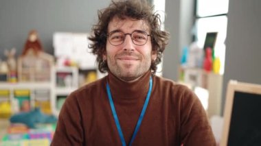 Young hispanic man preschool teacher smiling confident doing ok gesture at kindergarten