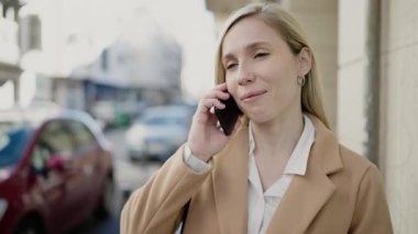 Genç sarışın kadın gülümsüyor. Kendine güveni tam. Akıllı telefondan konuşuyor.