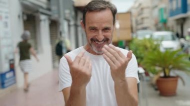 Middle age man smiling confident doing coming gesture with hand at street