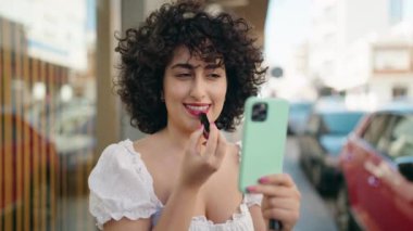 Orta Doğulu genç kadın makyaj dudakları sokakta akıllı telefon gibi görünüyor.