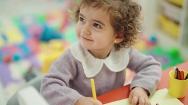 Adorable hispanic girl preschool student sitting on table drawing on paper at kindergarten