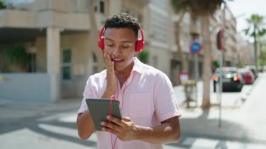 Young latin man watching video on touchpad at street