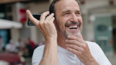 Middle age man smiling confident listening audio message by the smartphone at street