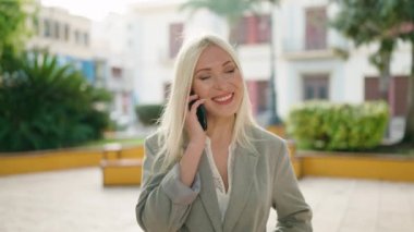 Genç sarışın kadın yönetici parkta akıllı telefondan konuşuyor.