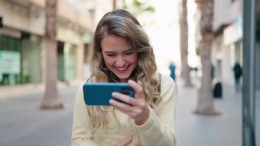 Sokakta akıllı telefondan video izleyen genç sarışın kadın turist.