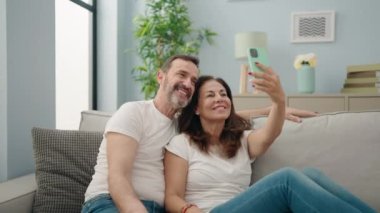 Erkek ve kadın çiftin akıllı telefonlarıyla evdeki kanepede selfie çekmesi.