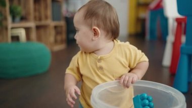 Adorable hispanic baby playing with construction blocks sitting on floor at kindergarten