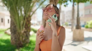 Young beautiful hispanic woman talking on the smartphone eating ice cream at park