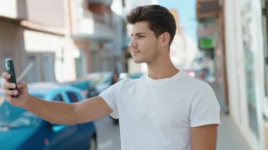 Genç İspanyol adam gülümsüyor. Parktaki akıllı telefonun yanında özçekim yapıyor.