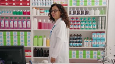 Middle age woman pharmacist smiling confident standing with arms crossed gesture at pharmacy