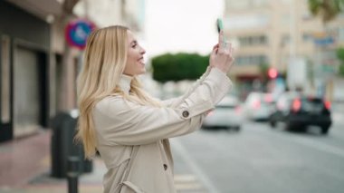 Young blonde woman smiling confident making selfie by the smartphone at street