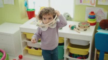 Adorable hispanic girl playing tambourine standing at kindergarten