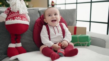 Tapılası İspanyol bebek elinde noel balosu ile evdeki kanepede oturuyor.