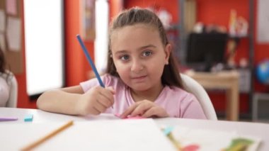 Adorable hispanic girl student sitting on table drawing on notebook at classroom