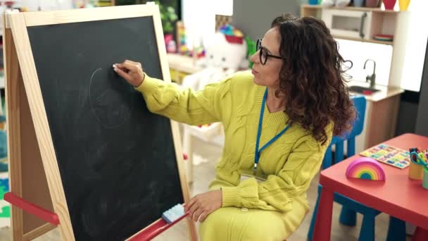 在幼儿园的黑板上画画的中年惊慌失措的幼儿园女教师 — 图库视频影像
