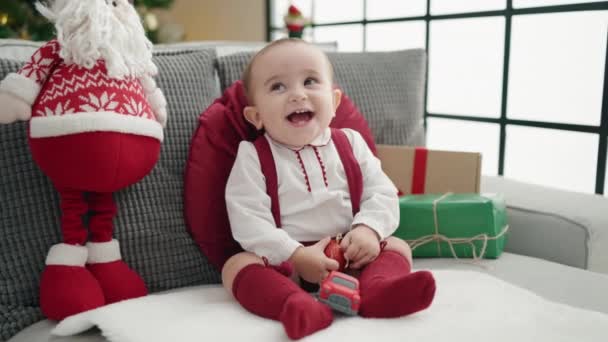 Αξιολάτρευτο Ισπανόφωνο Μωρό Κρατώντας Χριστουγεννιάτικη Διακόσμηση Μπάλα Κάθεται Στον Καναπέ — Αρχείο Βίντεο