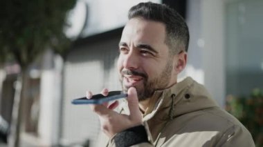 Young hispanic man smiling confident sending voice message by smartphone at street