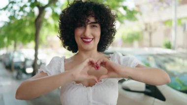 Young middle east woman smiling confident doing heart gesture with hands at street