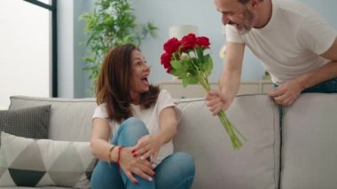 Kadın ve erkek, evdeki kanepede oturan çiçeklerle sürpriz yapıyor.