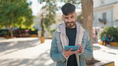 Young hispanic man smiling confident using touchpad at park