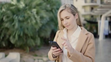 Parkta akıllı telefon kullanan, kendine güvenen genç sarışın kadın.