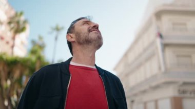 Orta yaşlı, rahat yüzlü, gökyüzüne bakan bir adam.